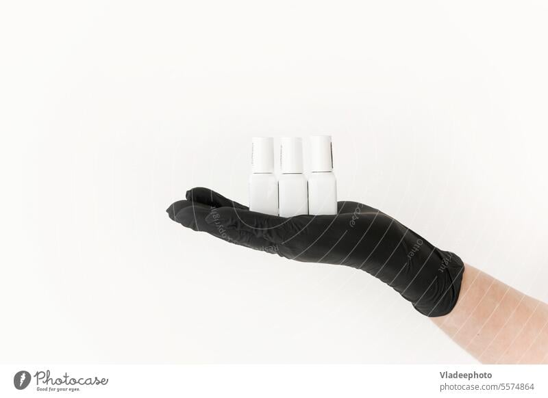 White Jars with Nail Polish on the Palm in a Black Nitrile Glove on a White Background. Manicurists jar nail varnish polish hand glove black woman stylish