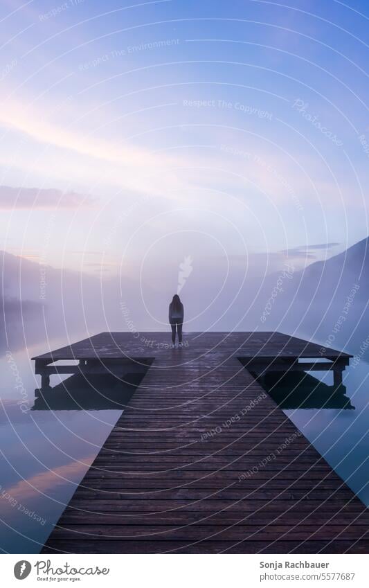 Rear view of a woman on a wooden jetty by the lake. Sunrise. Woman Lake Water Lakeside Calm Environment wooden walkway Nature Sky Autumn Exterior shot Idyll