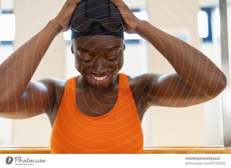 Black young woman smiling while putting on her swimmin hats sitting at the changing female person black swimming pool heated swimsuit orange happy blue