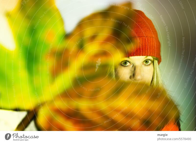 An expectant woman with a cap hidden behind an autumn leaf Woman Autumn Young woman Autumnal Leaf Autumnal colours blurred Cap blonde hair eyes Red