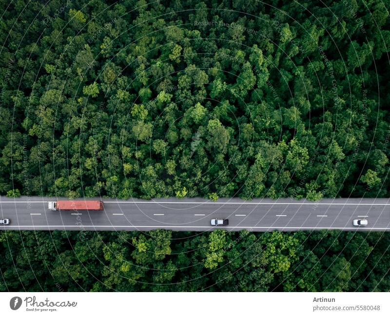 Aerial top view of car and truck driving on highway road in green forest. Sustainable transport. Drone view of hydrogen energy truck and electric vehicle driving on asphalt road through green forest.