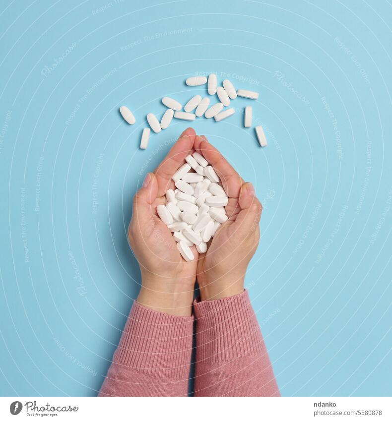 Two female hands hold white oval pills on a blue background, top view woman holds medication health care drugs dose concept wellness treatment pharmaceutical