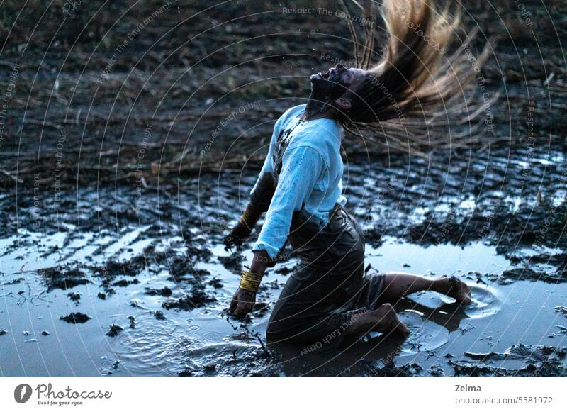 Dramatic portrait of a young woman kneeling in the black mud on field, cry of despair desperate scream dramatic hair dreadlocks muddy stress depression golden