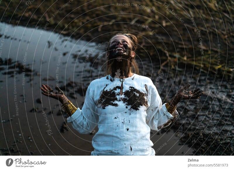 A happy authentic woman stuck in a mud puddle in a field dirty hands face outdoor cheerful joy freedom daring spirit beautiful dress witch sorceress natural