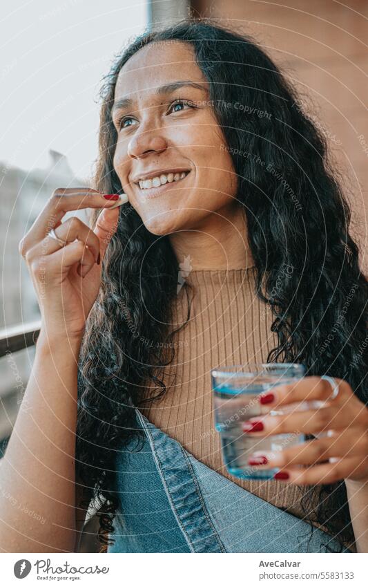 Diverse woman sitting at home and taking painkillers pills, working on laptop, freelancer concept. supplement happy vitamin healthy laughing stylish lady model