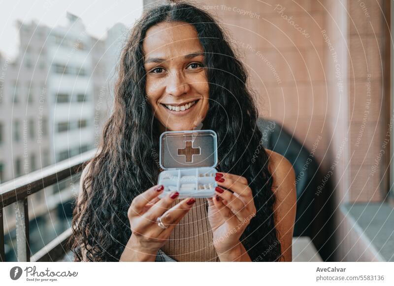 Diverse woman sitting at home showing pills to camera, working on laptop, freelancer concept. supplement happy painkiller vitamin healthy laughing african smile