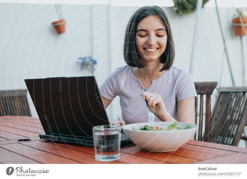 Young freelancer woman working on laptop and eating salad, healthy people, working at home concept. pill supplement happy painkiller vitamin typing wireless