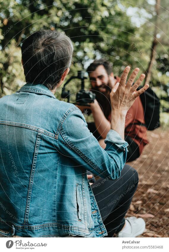 Senior jubilant woman explaining her trip to followers while a guy records her live on social media. mental health streamer video senior retirement person