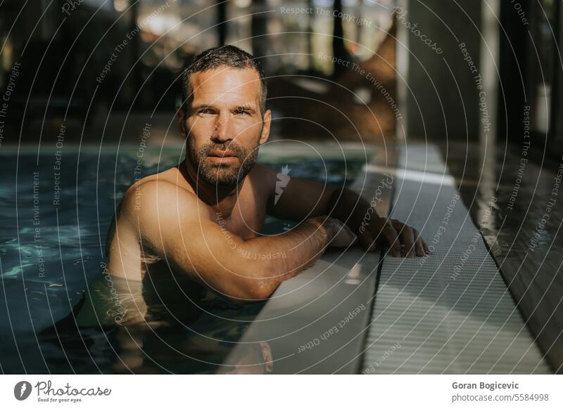 Handsome young man relaxing on the edge of indoor swimming pool caucasian fitness attractive water adult athletic male handsome strong activity vacation leisure