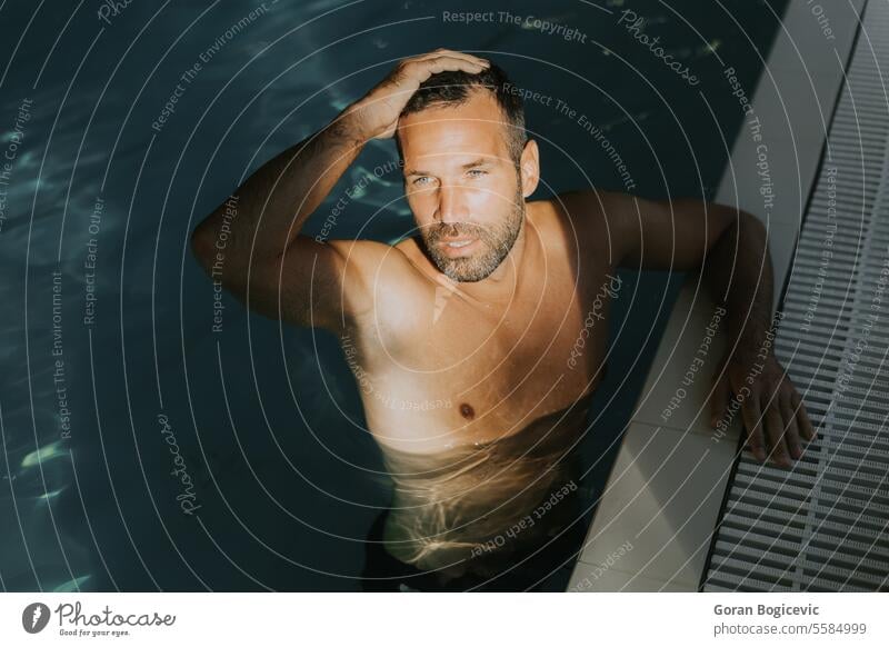 Handsome young man relaxing on the edge of indoor swimming pool caucasian fitness attractive water adult athletic male handsome strong activity vacation leisure