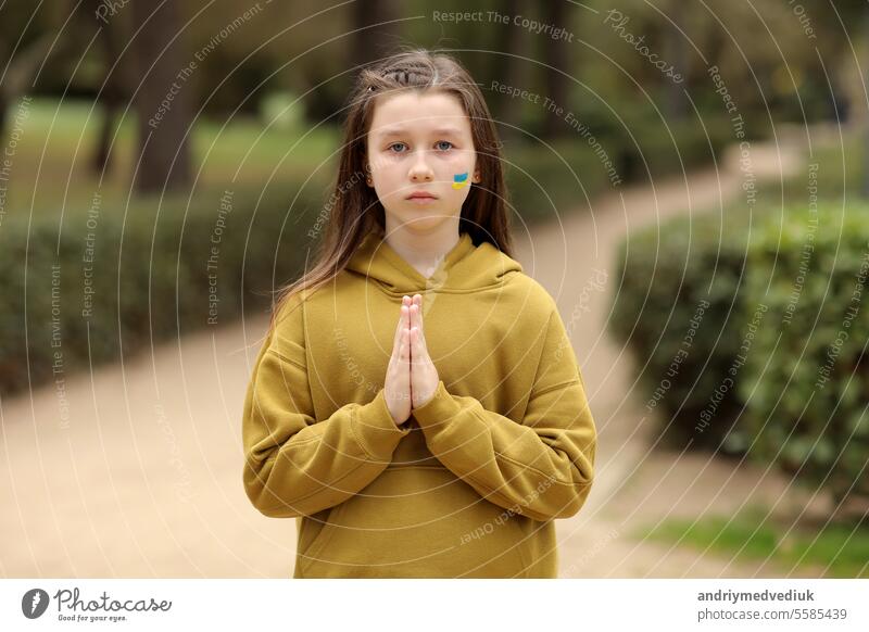 A sad child Ukrainian girl with the flag of Ukraine on her face is praying. The concept of participation of the Ukrainian people in the war with Russia. Not war concept. children ask for peace