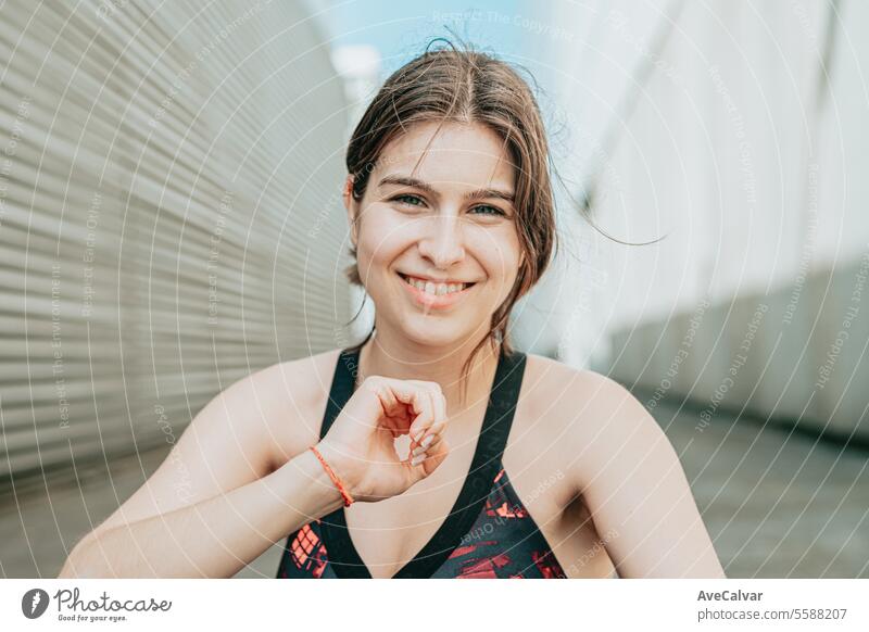 Portrait of a young girl smiling at camera in sportswear touching her hair in an urban setting. female person women happy caucasian portrait beauty cheerful