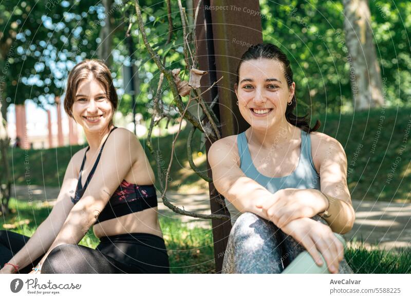 Two friends resting and talking while sitting after a hard workout leaning on tree.Sport in the city summer person female lifestyle two young park outdoors