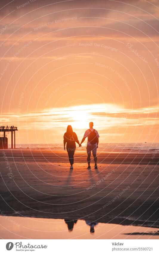 Romantic walk of a young couple on the beaches of Oostende in western Belgium at sunset. Love and devotion. Reflection in a pool of water woman honeymoon