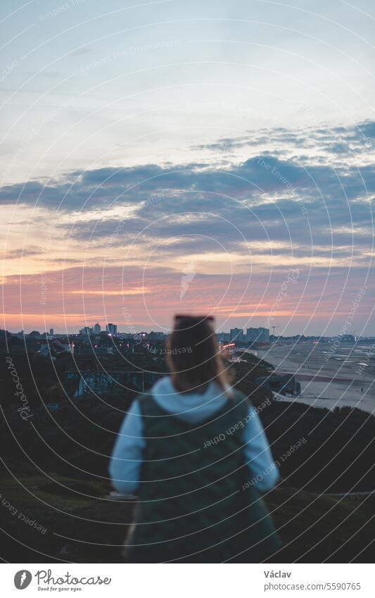 View of the city of Dunkirk from a military base during World War II. A blurry woman watching the sun set over a sad place. France stylish blurred tourist bokeh