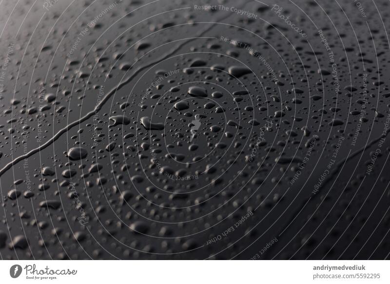 Rain or water drops different size on a black shiny car hood surface. Water droplets on dark iron surface and texture. Abstract background and water texture for design.