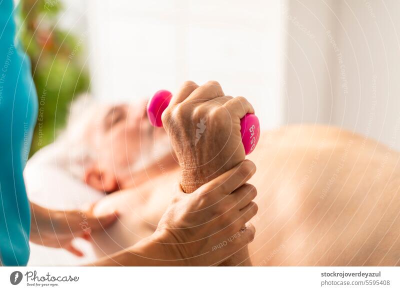 An older, retired man receives a physiotherapy and rehabilitation session, using light weights, to treat a problem in his wrist and arm joint physiotherapist