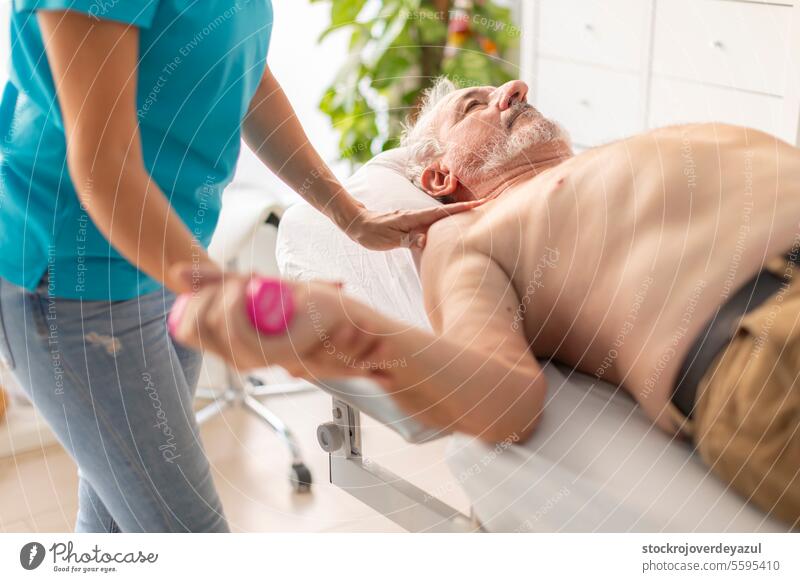 An older, retired man receives a physiotherapy and rehabilitation session, using light weights, to treat a problem in his wrist and arm joint physiotherapist