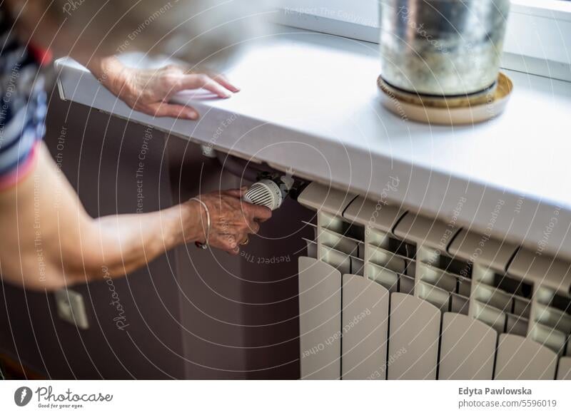 Senior woman adjusting thermostat on the radiator at home real people senior mature female Caucasian elderly house old aging domestic life grandmother pensioner