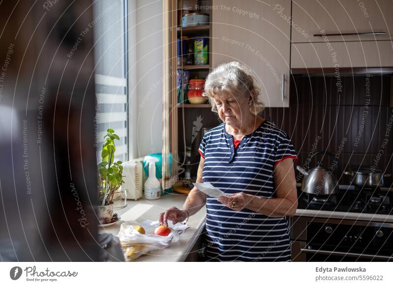 Senior woman going through her receipts at home after buying groceries shopping counting money bills cost of living costs worried financial planning finance