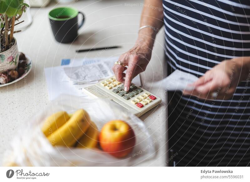 Senior woman going through her receipts at home after buying groceries shopping counting money bills cost of living costs worried financial planning finance