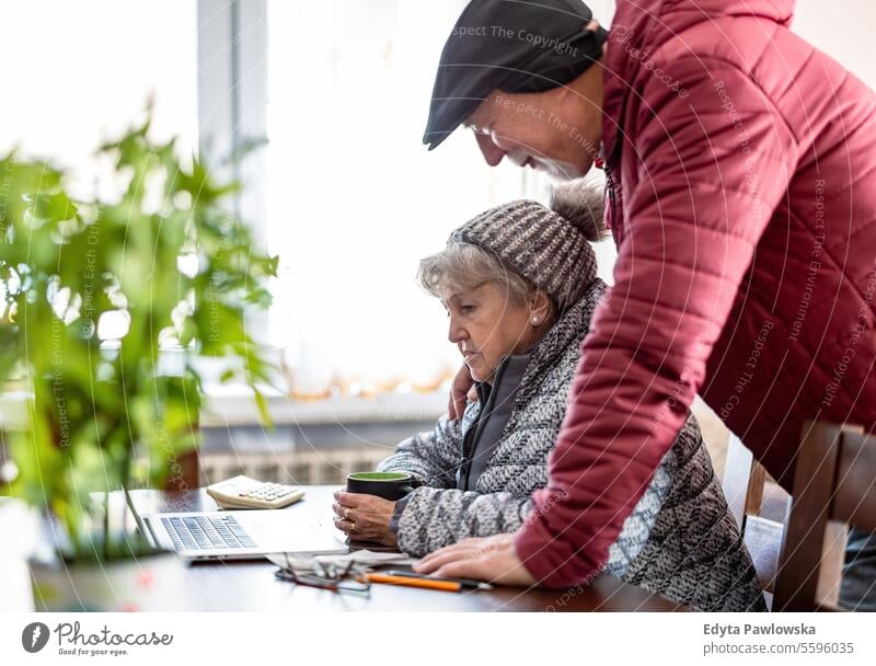 Senior couple in winter clothing going over their energy bills on laptop at home cold temperature warm clothing uncomfortable sadness frozen energy efficient