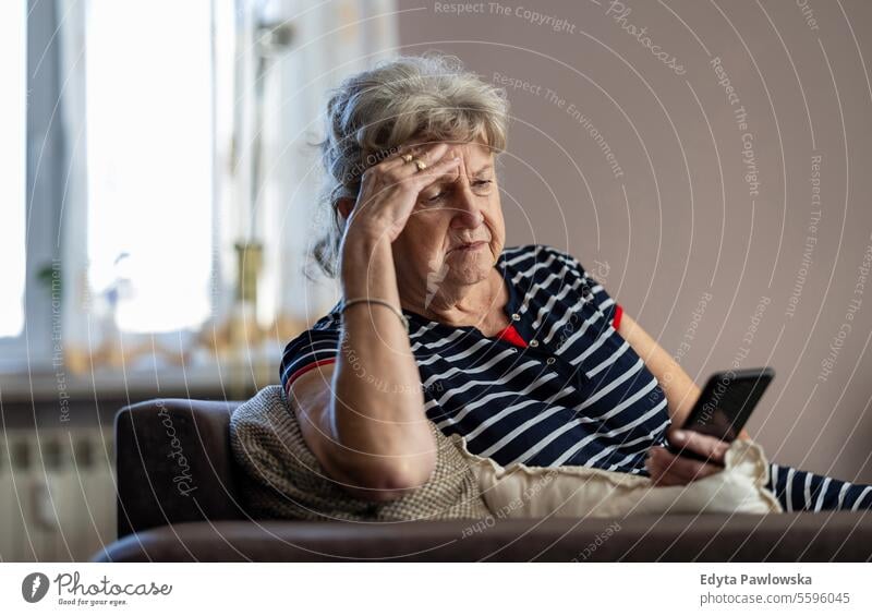 Elderly woman sitting on couch and using mobile phone at home real people senior mature female Caucasian elderly house old aging domestic life grandmother