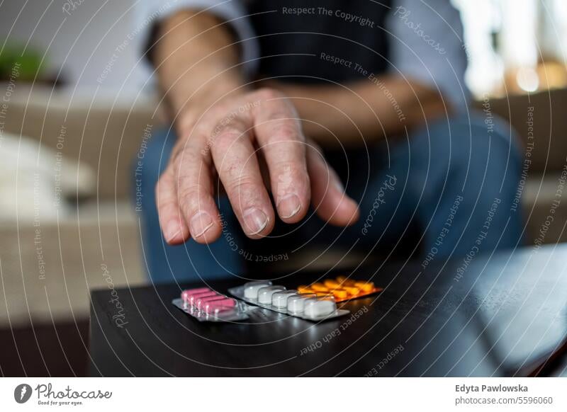 Close-up of man taking pills on sofa at home in the living room real people senior senior adult mature male Caucasian elderly house old aging domestic life