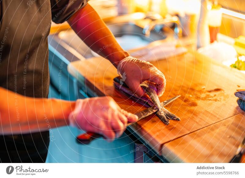 Crop anonymous cook in black uniform and gloves with knife standing at counter while preparing seafood at nightclub man meat slicing prepare bar chef modern