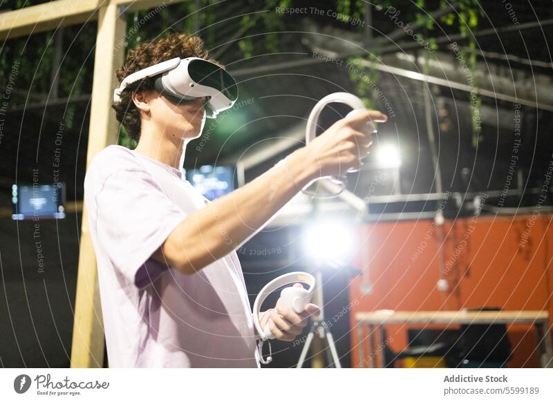 Side view of young excited man is engaged in a virtual reality game wearing a VR headset and using controllers technology vr goggles gadget entertainment