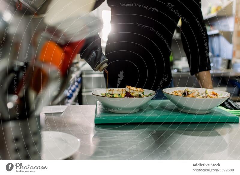 Crop anonymous male chef in black uniform serving delicious salad with grilled cheese in kitchen of restaurant man serve cook food culinary prepare tasty