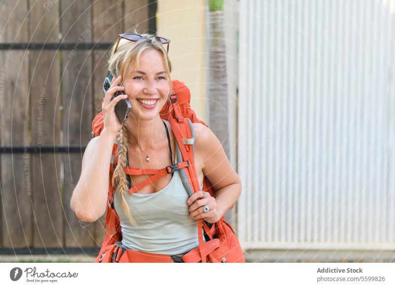 Cheerful Young woman with backpack talking on smartphone adventure blurred background cheerful communicate conversation copy space countryside daylight daytime