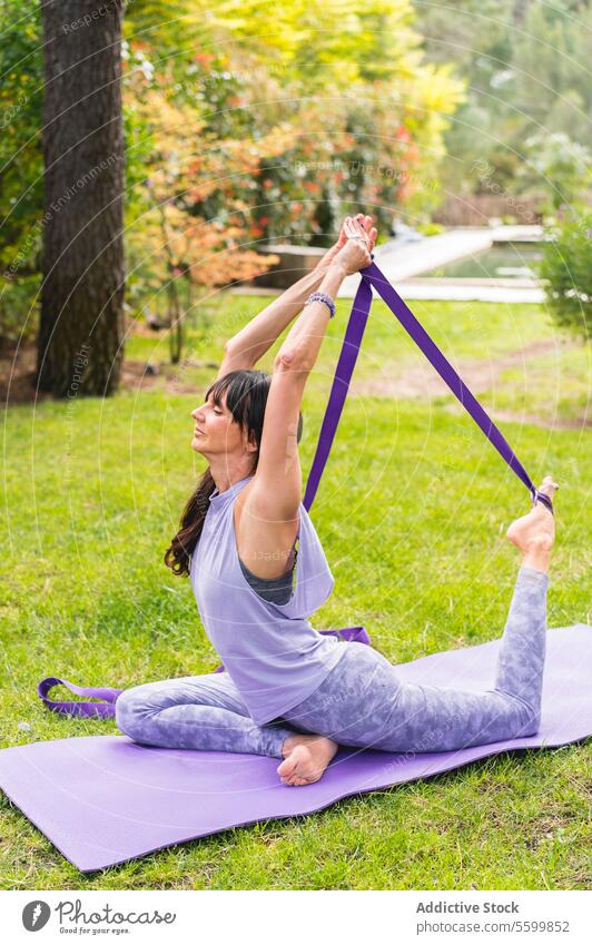 Mid adult female doing one-legged king pigeon pose with a strap. Body Care active lifestyle activity agility athlete backyard balance barefoot bending