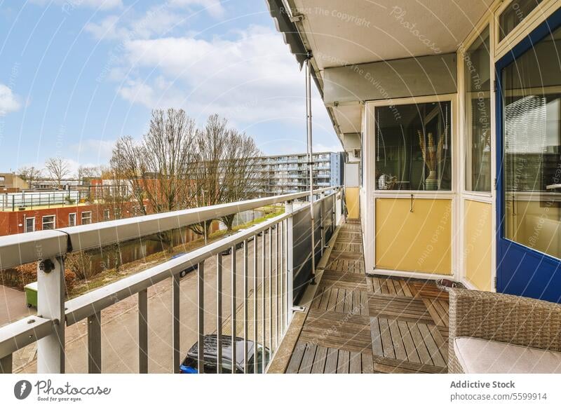 Narrow balcony of apartment against cloudy sky building narrow long empty tree door railing wood floor entrance terrace construction architecture daytime