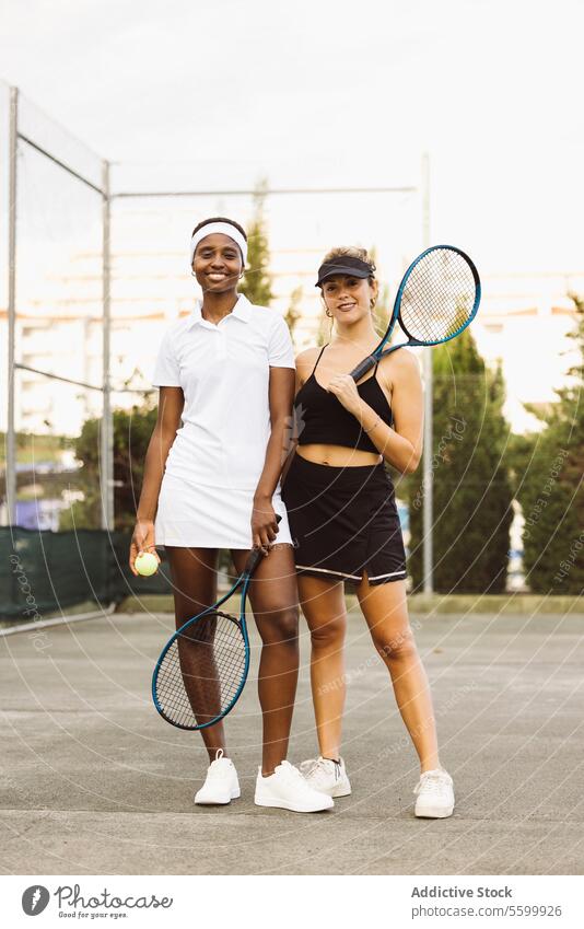 Portrait of two young women on a tennis court active lifestyle activity amateur athlete ball beautiful beautiful women cheerful competition diversity enjoyment