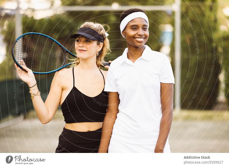 Portrait of two young women on a tennis court active lifestyle activity amateur athlete ball beautiful beautiful women cheerful competition diversity enjoyment