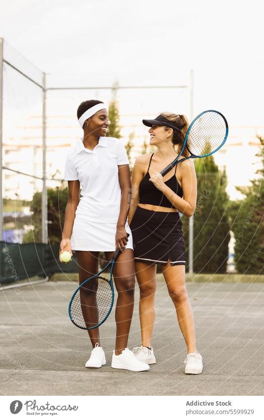 Portrait of two young women on a tennis court active lifestyle activity amateur athlete ball beautiful beautiful women cheerful competition diversity enjoyment