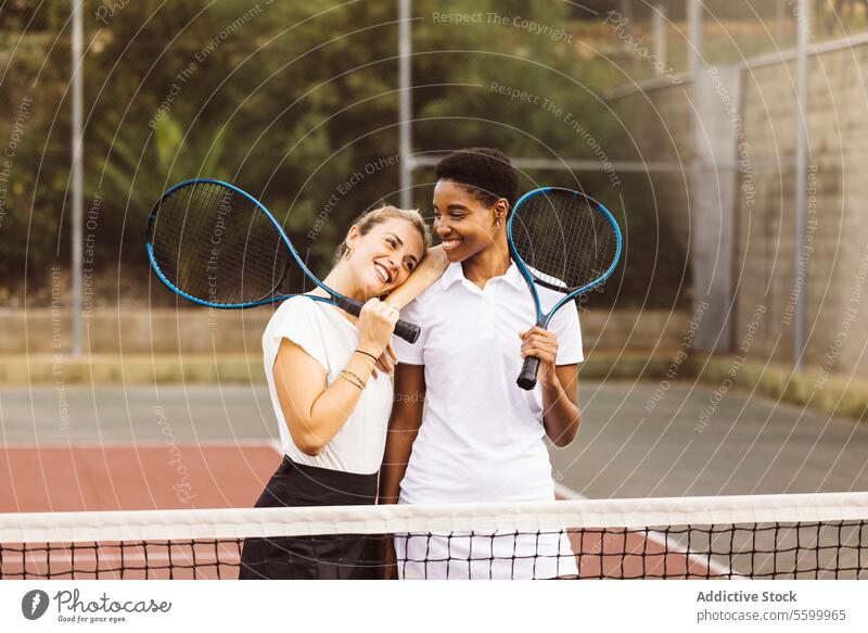 Portrait of two young women on a tennis court active lifestyle activity amateur athlete ball beautiful beautiful women cheerful competition diversity enjoyment