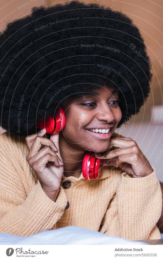 Smiling black woman listening to music with headphones earphones using bed rest home weekend chill female african american afro gadget relax device cheerful