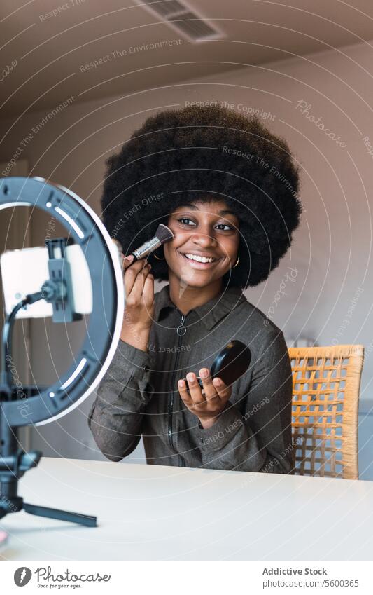 Black woman recording beauty video makeup tutorial cosmetic vlog smartphone ring lamp powder blog social media online afro leisure hairstyle feminine blogger