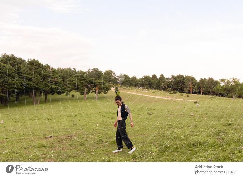 Happy man with bare chest strolling happily through a green field meadow lush tree horizon sky dusk nature outdoor explorer enjoying walk vast grassland leisure