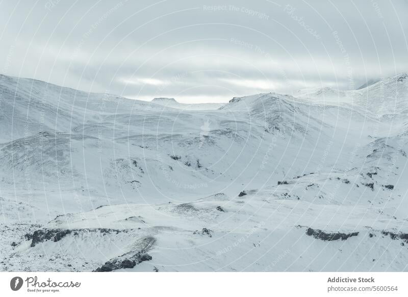 Aerial view of Snowy Mountain Expanse under Cloudy Sky snowy mountain expanse snow-blanketed plateau subtle sunlight subdued landscape nature winter cold