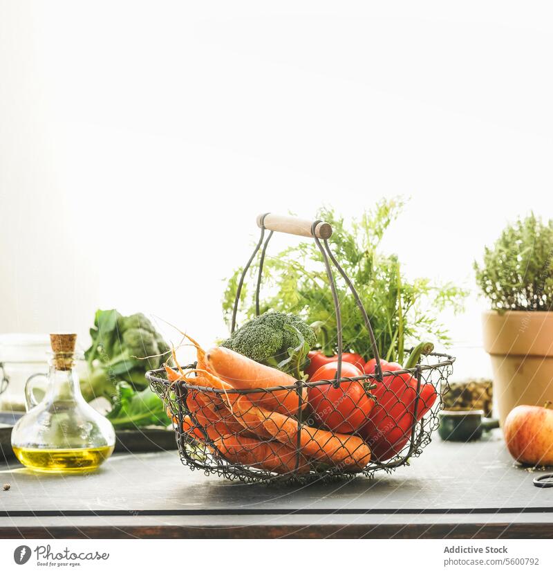 Metal grocery basket with organic vegetables: carrots, broccoli, bell pepper and tomatoes on table with other healthy ingredients at window background with sunlight. Healthy lifestyle. Front view.