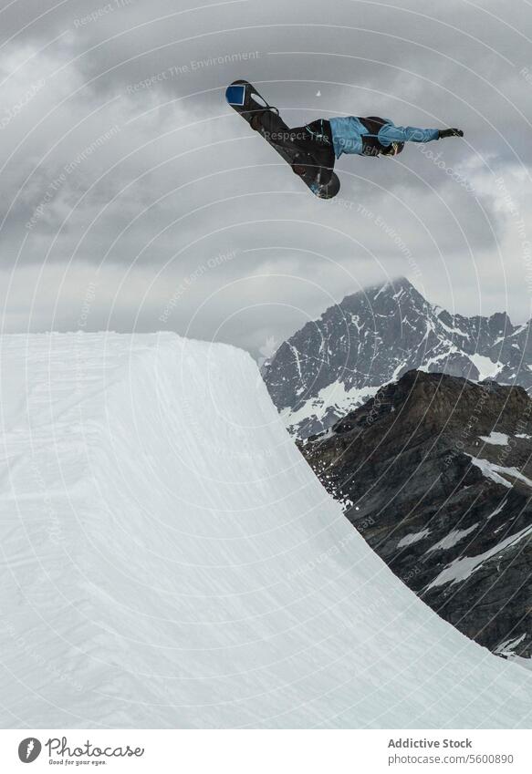 Side view of anonymous man with snowboard jumping on snowy mountain against cloudy sky during vacation at Swiss Alps peak full body nature active motion