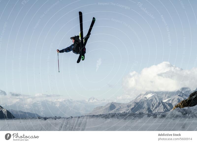 Anonymous carefree man skiing and jumping on snowy mountain while enjoying winter day at Swiss Alps skier active pole vacation adventure motion mid-air sky