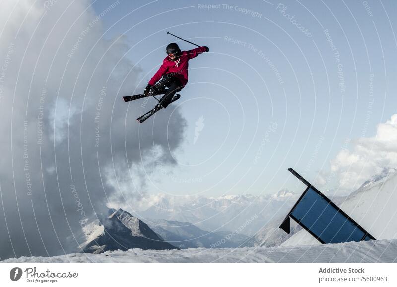 Anonymous carefree man skiing and jumping on snowy mountain while enjoying winter day at Swiss Alps skier active pole vacation adventure motion mid-air sky