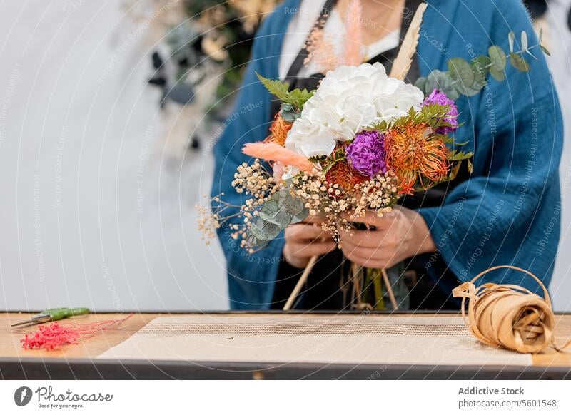 Anonymous person crafting a bouquet with flowers florist arrangement hydrangea bloom workshop table wooden apron blue assembling blossom vibrant white