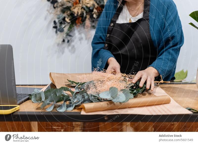 Florist preparing a bouquet at workshop table arrangement greenery creativity tools scissors laptop preparation flowers foliage eucalyptus design craft handwork