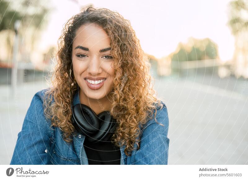 Smiling woman with wireless headphones on street smile happy cheerful style curly hair female positive city young enjoy portrait trendy lifestyle relax casual