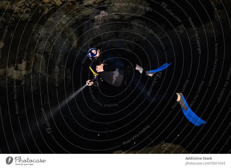 Anonymous Scuba Diver with fins, scuba gear and flashlight exploring Cenote Dos Ojos in Mexico exploration beams depths textured surfaces contours cavern